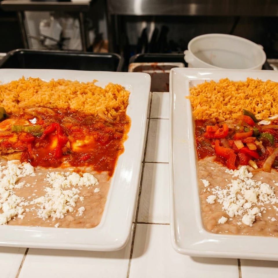 Two plates of huevos rancheros with rice, beans, salsa, and crumbled cheese in a kitchen.