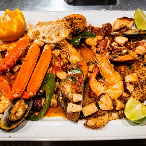 A large platter of seafood including crab legs, shrimp, mussels, octopus, and fish with lime and orange garnishes.